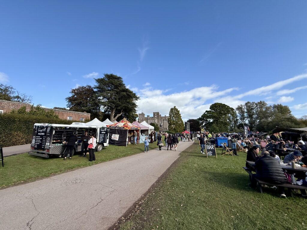 Food and drink stalls with visitors on the lawn outside Powderham Castle during Powderham Food Festival.