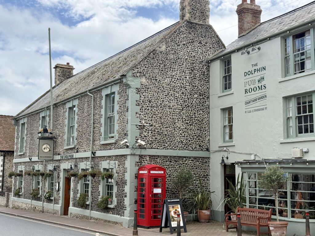 The Dolphin Hotel in Beer, Devon, beside traditional stone buildings and a red telephone box on Fore Street.