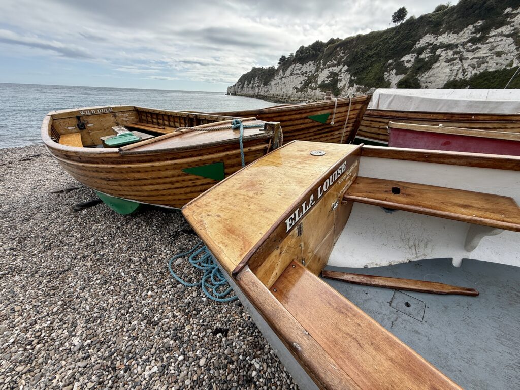 Wooden self drive motorboats available to hire on the shingle at Beer Beach, with white chalk cliffs behind.