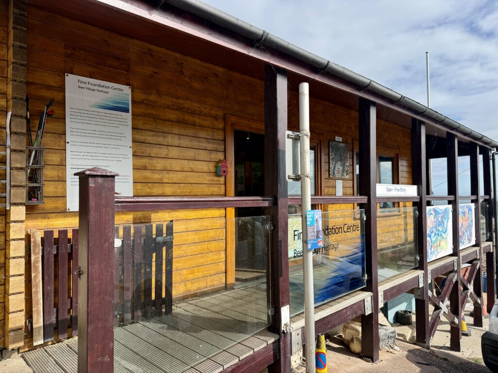 Wooden Fine Foundation Centre behind Beer Beach, home to Beer Village Heritage Centre, with its entrance and free admission sign.