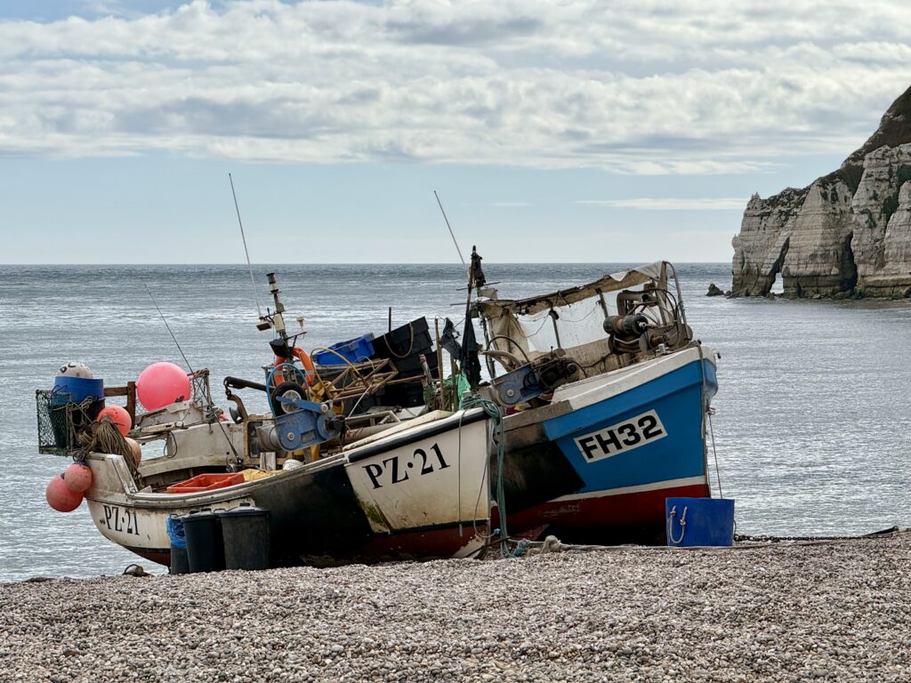 Traditional fishing boats pulled onto the shingle at Beer Beach, with the sea and white chalk cliffs behind.