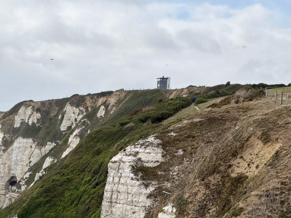 Walker following the South West Coast Path below the Lookout Tower on the white chalk cliffs of Beer Head, Devon.