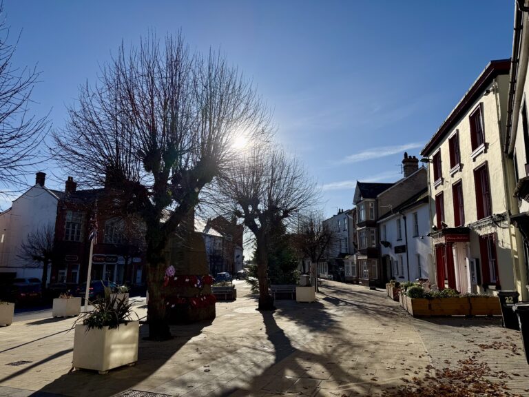 Higher Bull Ring in Cullompton on a sunny morning, with winter trees, pedestrian space and historic buildings in the town centre.