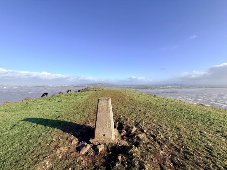 Ordnance Survey trig point at the highest point of Brean Down, with grazing cattle and the Somerset Levels visible to the east.