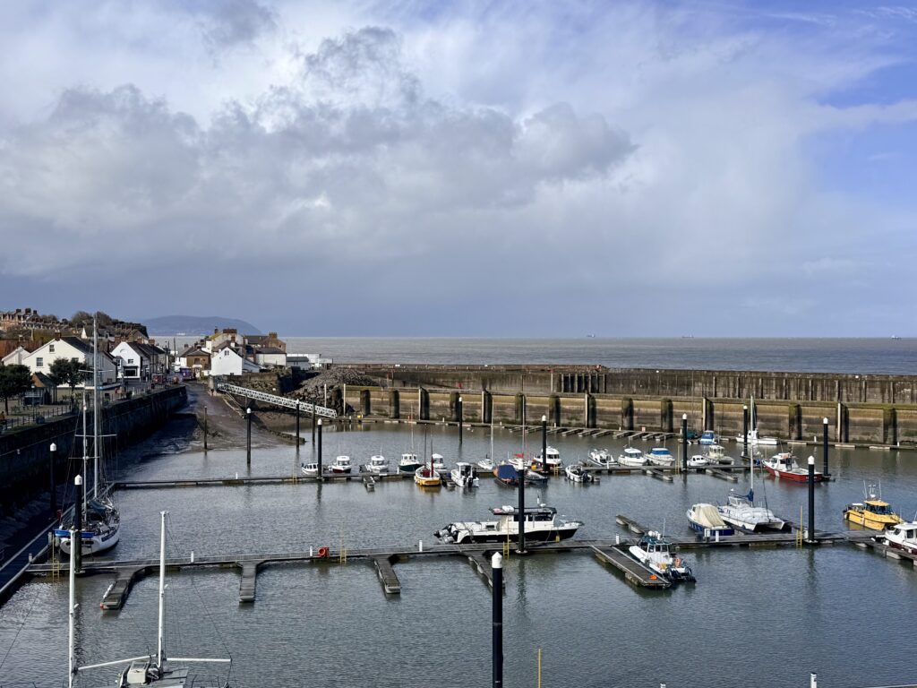Watchet Harbour and Marina in Somerset with moored boats, floating pontoons and tidal basin, historic harbour walls and Bristol Channel coastline beyond
