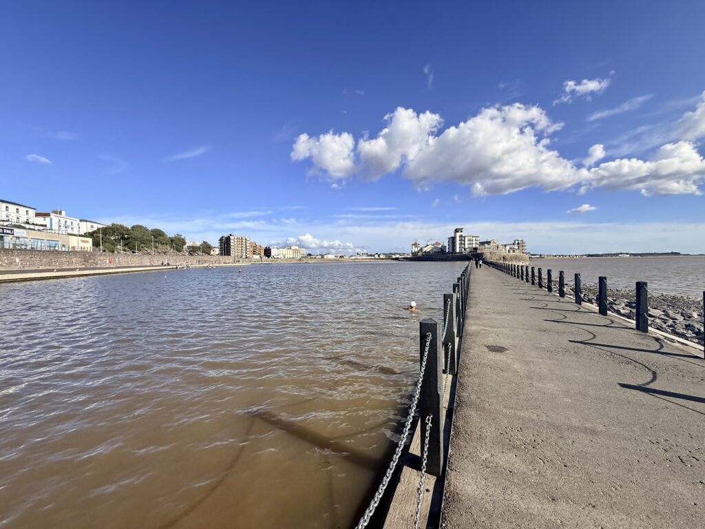 Swimmer in the Marine Lake at Weston-super-Mare, with the long causeway leading towards Knightstone Island and the Bristol Channel beyond under a bright blue sky.