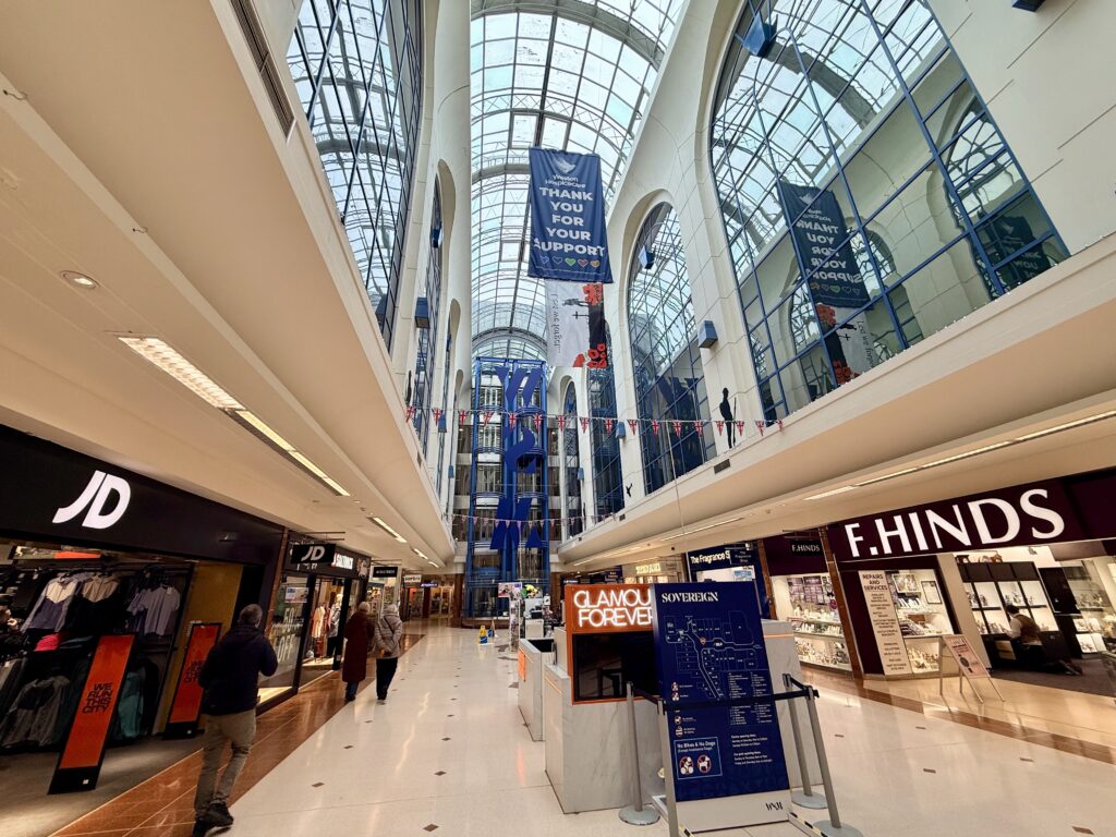 Interior of the Sovereign Shopping Centre in Weston-super-Mare showing shops, escalators and a glass roofed atrium in the town centre.
