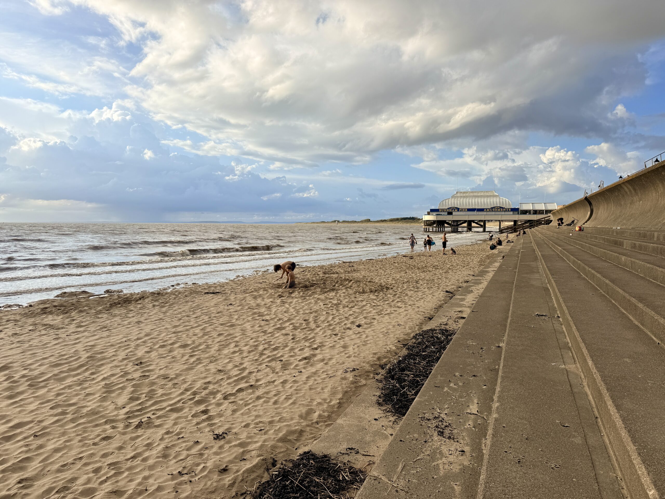 Burnham-on-Sea beach at high tide with the pier, sea wall and people on the sand.