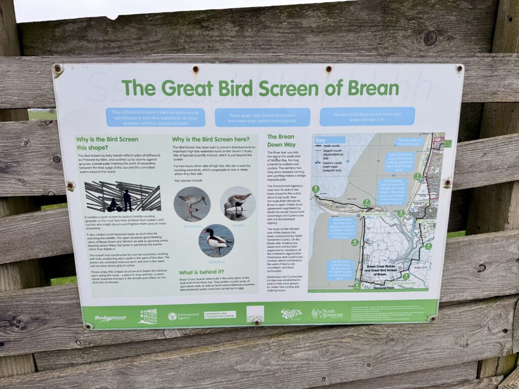 Close view of an information board titled “The Great Bird Screen of Brean” mounted on a wooden fence along the Brean Down Way, showing text, bird illustrations and a map explaining the estuary, wildlife and walking route.