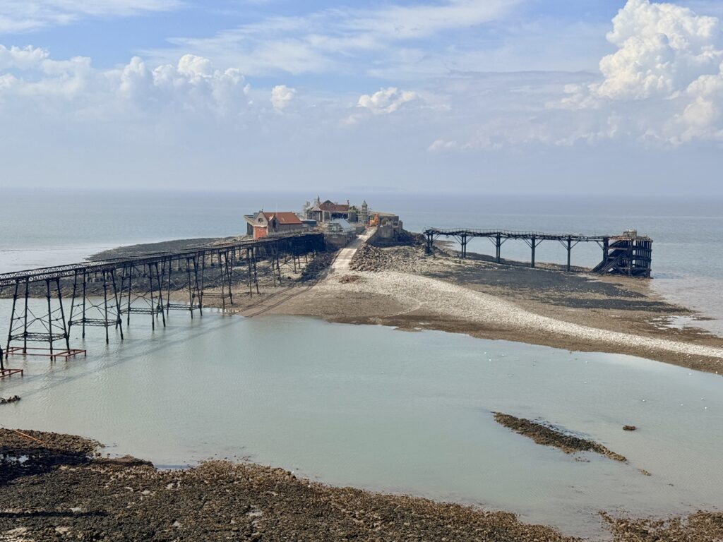 Birnbeck Pier at Weston-super-Mare at low tide, showing the historic pier buildings on Birnbeck Island and the damaged iron pier structure extending across the rocky foreshore.