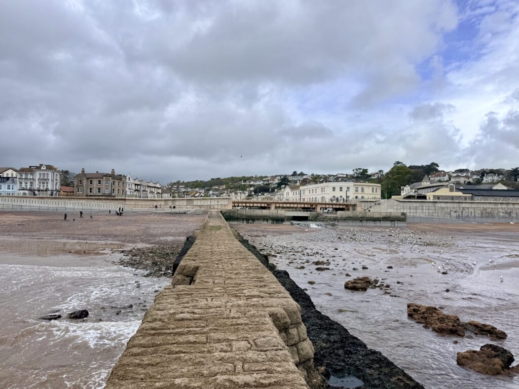 Dawlish, Devon at low tide with stone pier leading across the beach towards the town, seafront buildings and railway viaduct.
