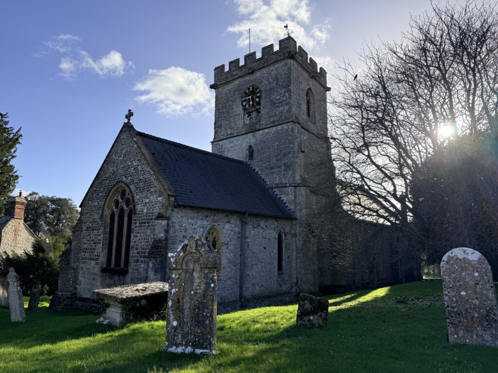 St Stephen’s Church, Winsham, Somerset, showing the stone tower, churchyard gravestones and afternoon sunlight through trees.