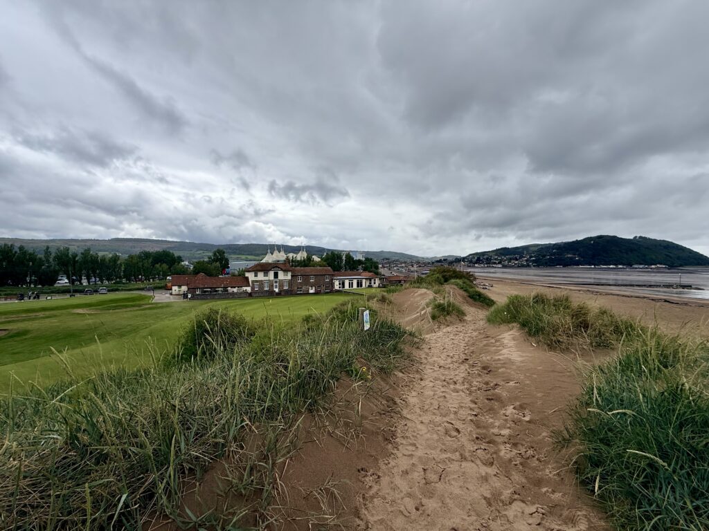 Sandy path through dunes approaching Minehead, with Minehead Golf Club on the left, Butlin’s Minehead in the distance and the Bristol Channel shoreline to the right.