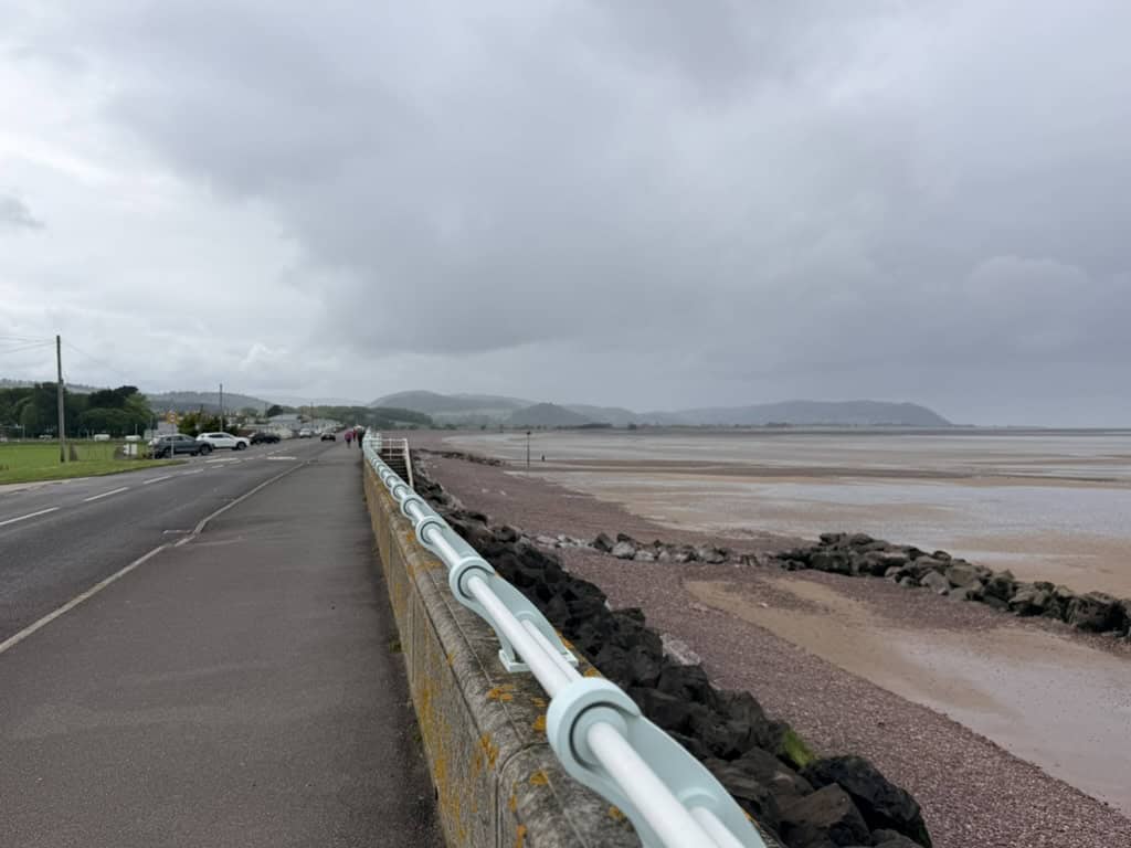 Blue Anchor promenade and beach at low tide, with shingle shoreline, sea wall and distant hills along the West Somerset coast path.