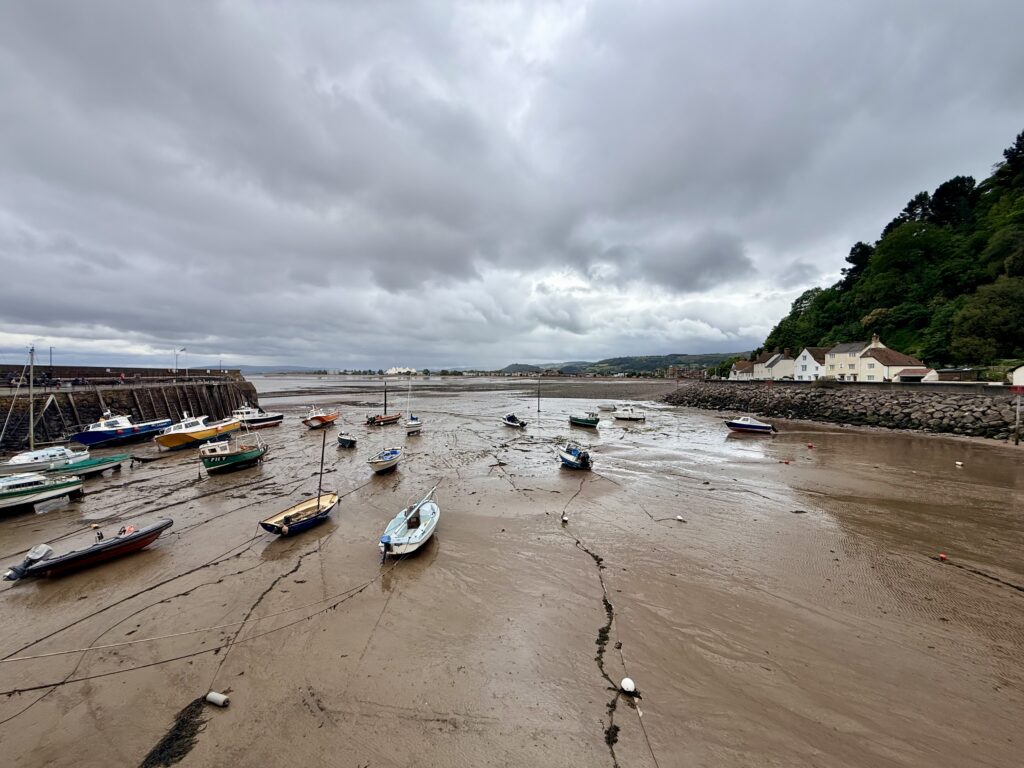 Minehead harbour at low tide with boats resting on sand, stone harbour wall and North Hill in the background, Somerset coast