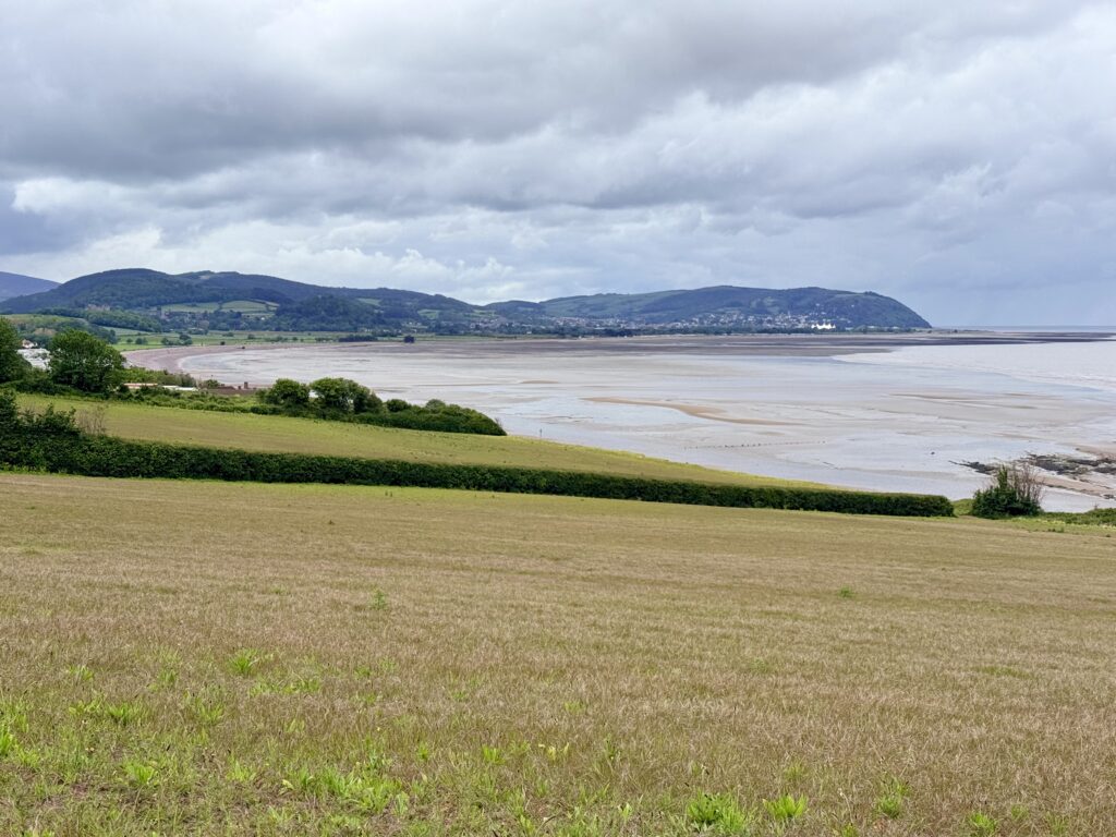 Wide coastal view from Blue Anchor on the Watchet to Minehead walk, looking west towards Dunster Beach and Minehead, with the Bristol Channel and Brendon Hills in the background.