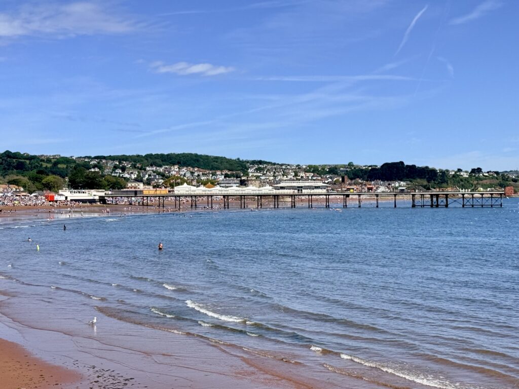 Paignton Sands and Paignton Pier viewed from Paignton Harbour with the wide sandy beach and calm waters of Torbay on a sunny day.
