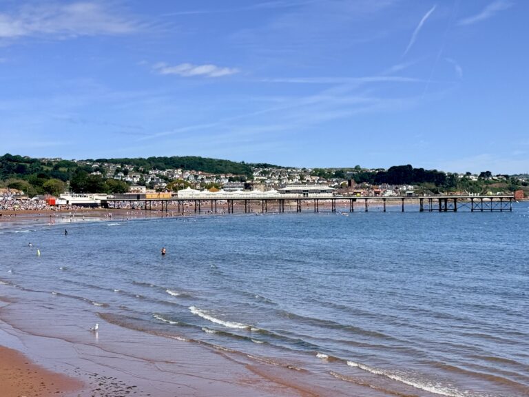 Paignton Sands and Paignton Pier viewed from Paignton Harbour with the wide sandy beach and calm waters of Torbay on a sunny day.
