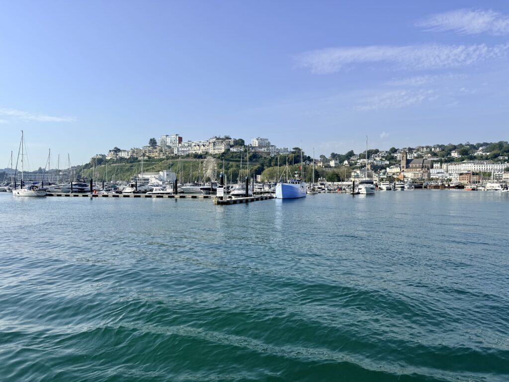 View of Torquay from the ferry across Torbay showing the marina, waterfront, hillside buildings and church on the English Riviera on a sunny day.