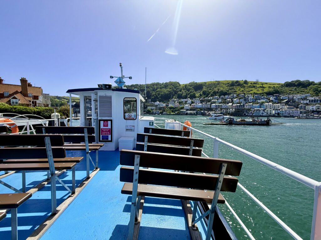 View from the Dartmouth to Kingswear passenger ferry, with the Lower Car Ferry crossing the River Dart and Dartmouth waterfront in the background.