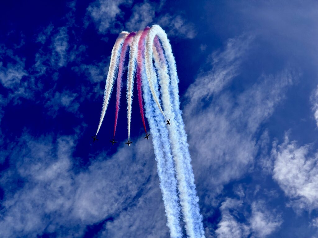RAF Red Arrows performing an aerobatic display with red, white and blue smoke trails at a UK airshow.