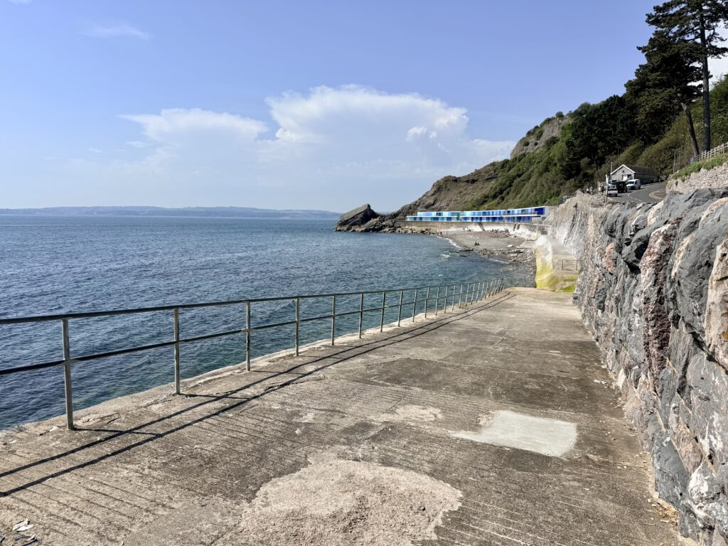 Meadfoot Beach in Torquay at high tide showing the slipway, rocky shoreline and colourful beach huts on the English Riviera.