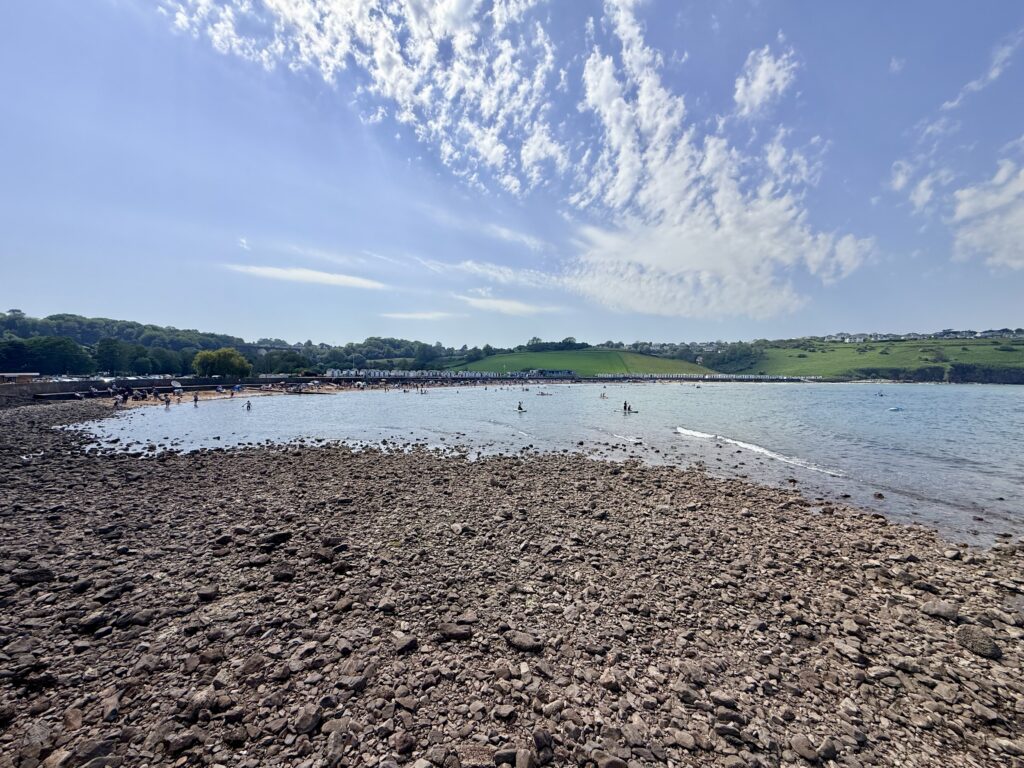 Broadsands Beach in Paignton showing the broad sandy bay, rocky foreshore at low tide and calm waters of Torbay on a sunny day.