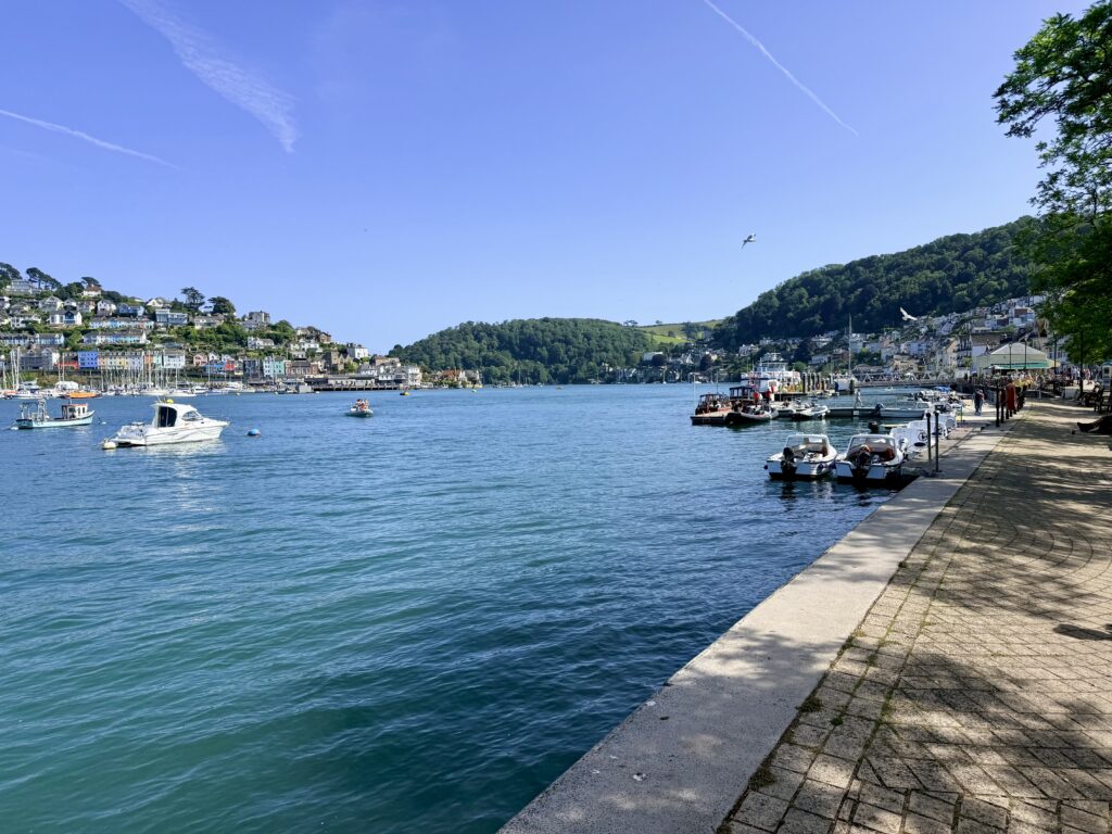 The Esplanade beside Dartmouth Harbour, with boats on the River Dart and wooded hills rising above the water in South Devon.