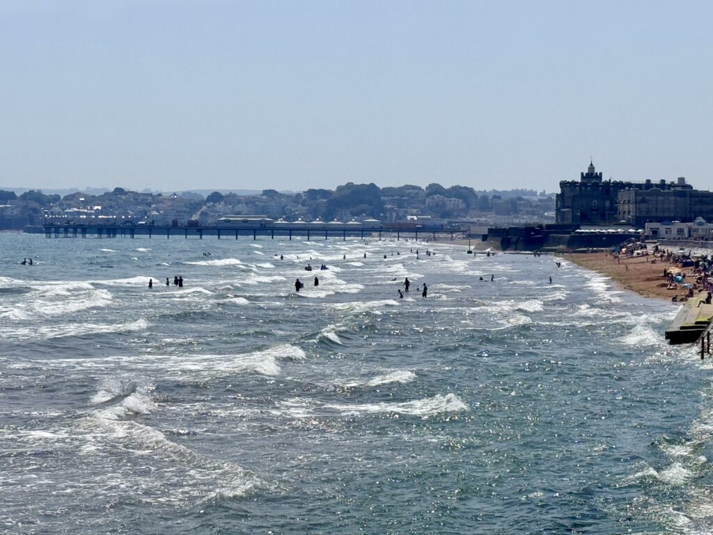 Preston Sands and Paignton Pier on the English Riviera with people enjoying the beach and swimming in Tor Bay on a summer day.