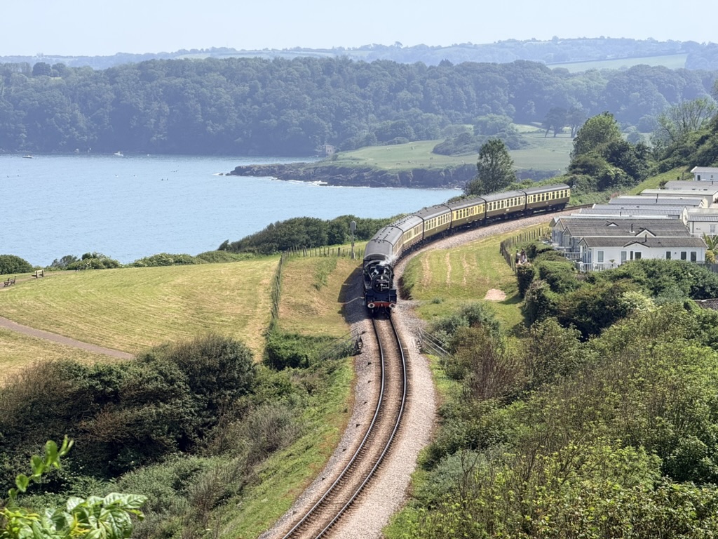 The Dartmouth Steam Railway climbing above Goodrington Sands with the South West Coast Path, Broadsands Beach and the coastline towards Elberry Cove on the shores of Torbay.