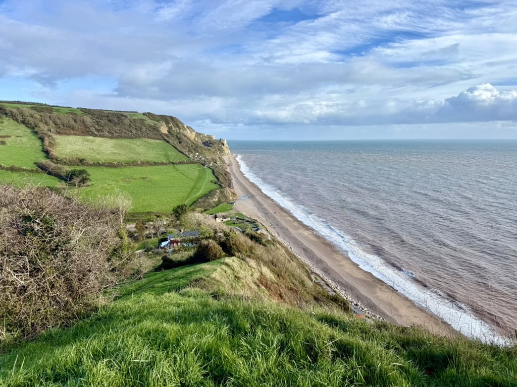 The East Devon coast at Branscombe, showing dramatic Jurassic Coast cliffs, rolling countryside and the long pebble beach stretching along Lyme Bay.