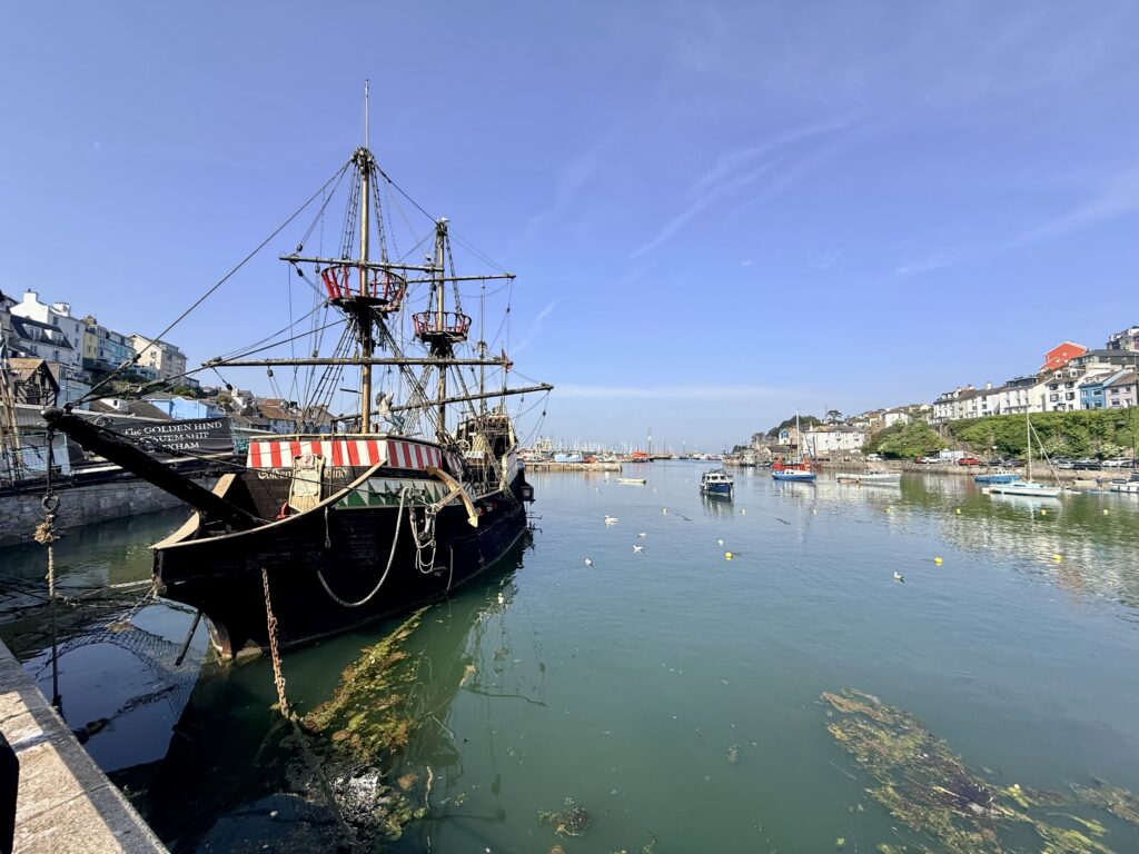 Replica of the Golden Hind moored in Brixham Harbour with fishing boats, the marina and colourful waterfront buildings on the English Riviera.