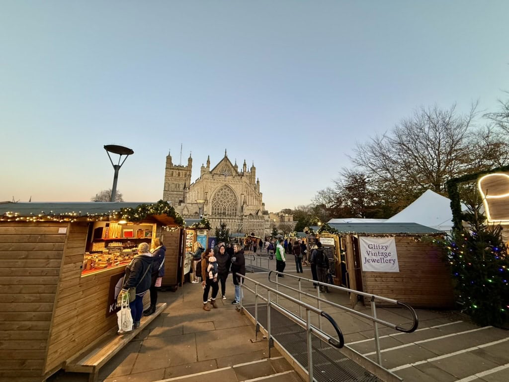 Exeter Christmas Market chalets and visitors on Cathedral Green, with Exeter Cathedral beyond