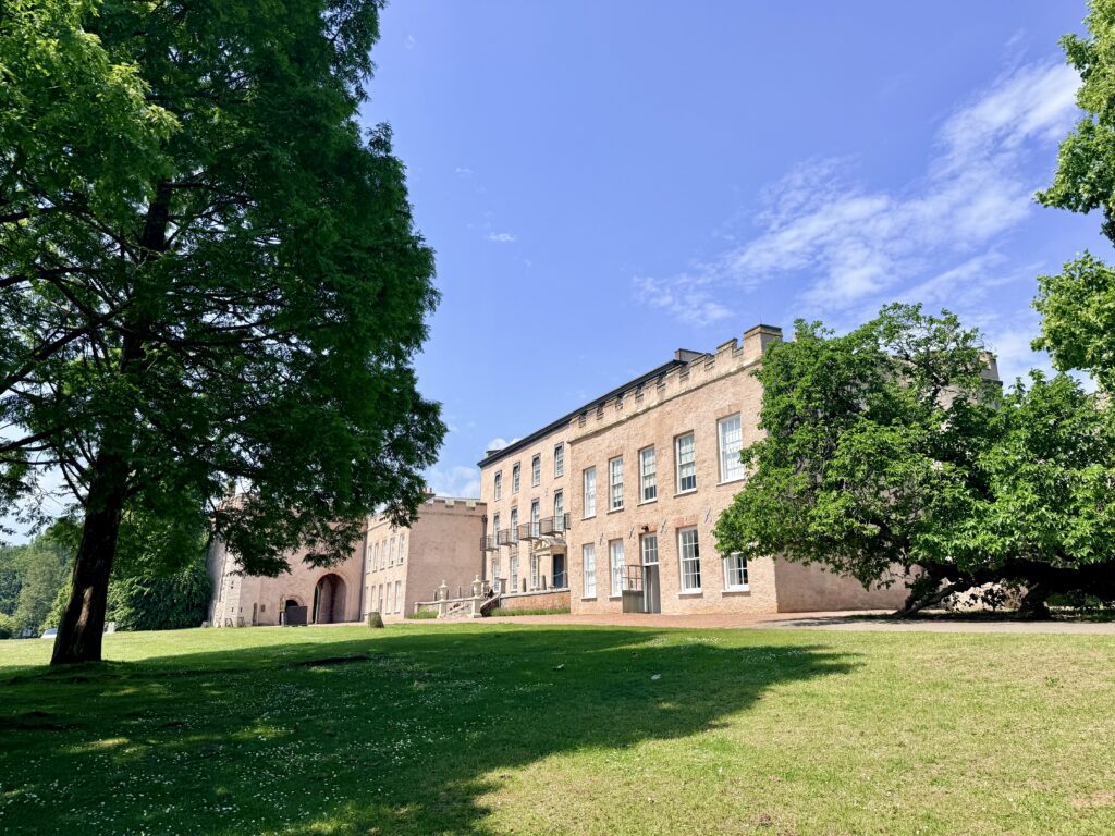 Historic pale stone façade of Torre Abbey in Torquay, surrounded by mature trees and sunlit lawns beneath a blue sky