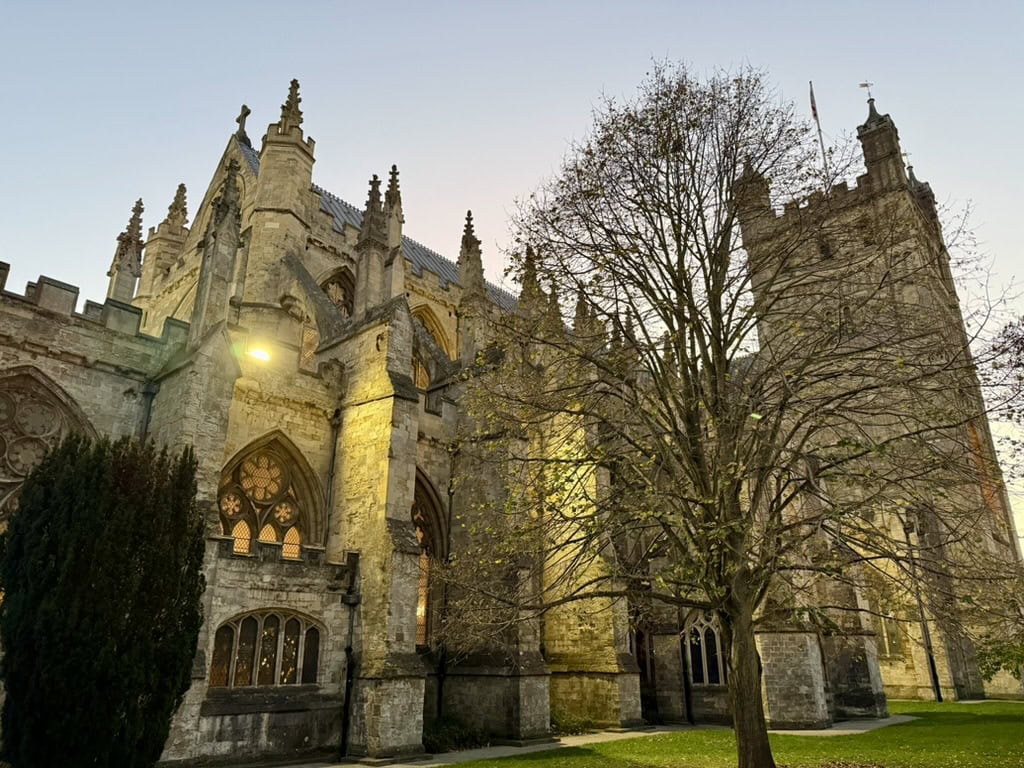 Historic stone walls, Gothic windows and tower of Exeter Cathedral illuminated at dusk