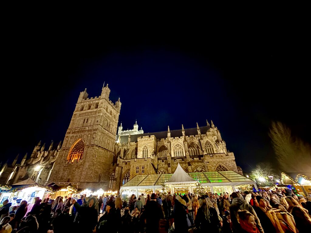 Crowds at Exeter Christmas Market beneath the illuminated Exeter Cathedral after dark