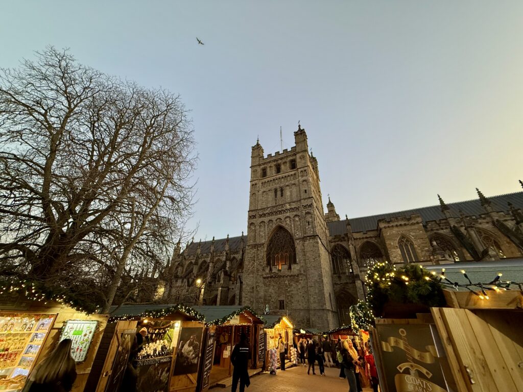 Illuminated Christmas Market chalets beneath the west front and tower of Exeter Cathedral