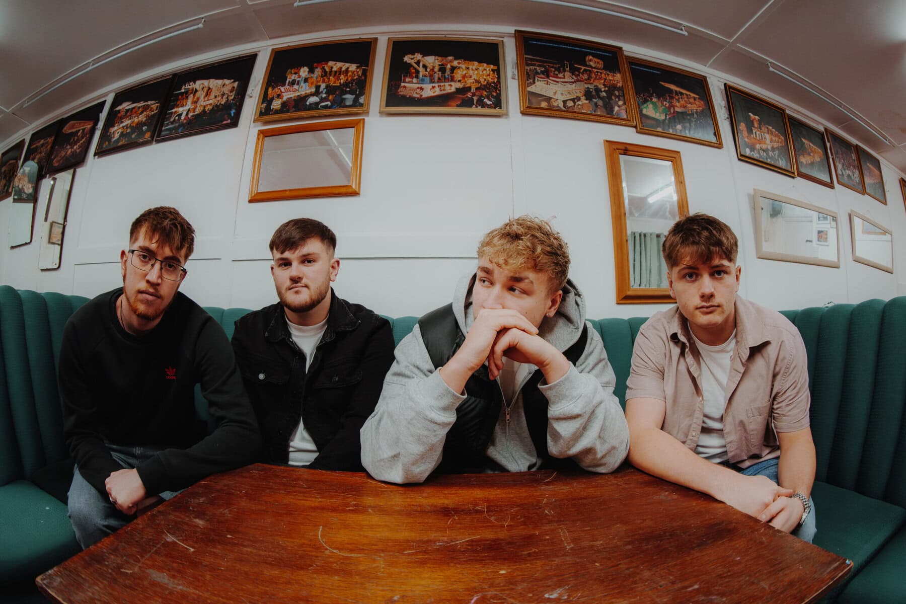 Four members of Bridgwater indie band Rosary Drive sitting around a wooden table beneath framed pictures, photographed through a wide angle lens.