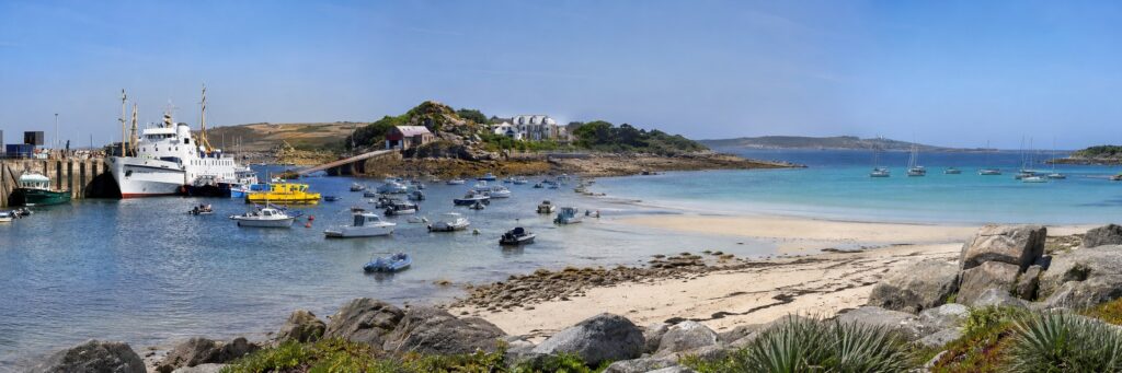 Panoramic collage of the Isles of Scilly showing Scillonian III in the harbour, small boats, a sandy beach, granite rocks and clear blue water.