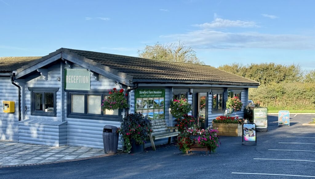 Stowford Farm Meadows reception building with colourful hanging baskets, flower displays and parking area.