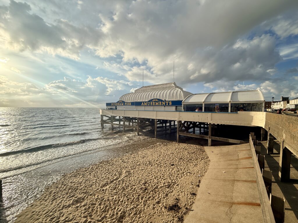 Burnham-on-Sea Pier extending over the sandy beach, with the Bristol Channel and promenade beneath a dramatic cloudy sky.