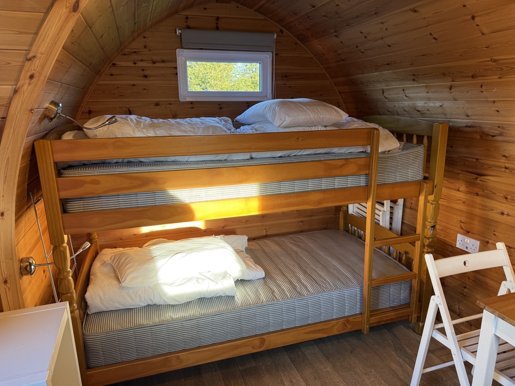 Wooden bunk beds with mattresses, pillows and reading lights inside a camping pod at Stowford Farm Meadows.