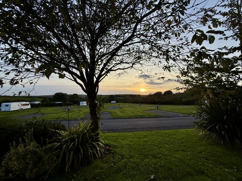 Sunset over the spacious touring pitches at Stowford Farm Meadows, with caravans, trees and the North Devon countryside.