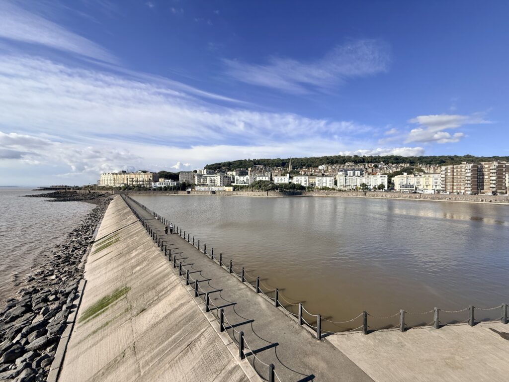 Marine Lake at Weston-super-Mare with the sea wall, waterfront buildings and wooded hillside beyond.