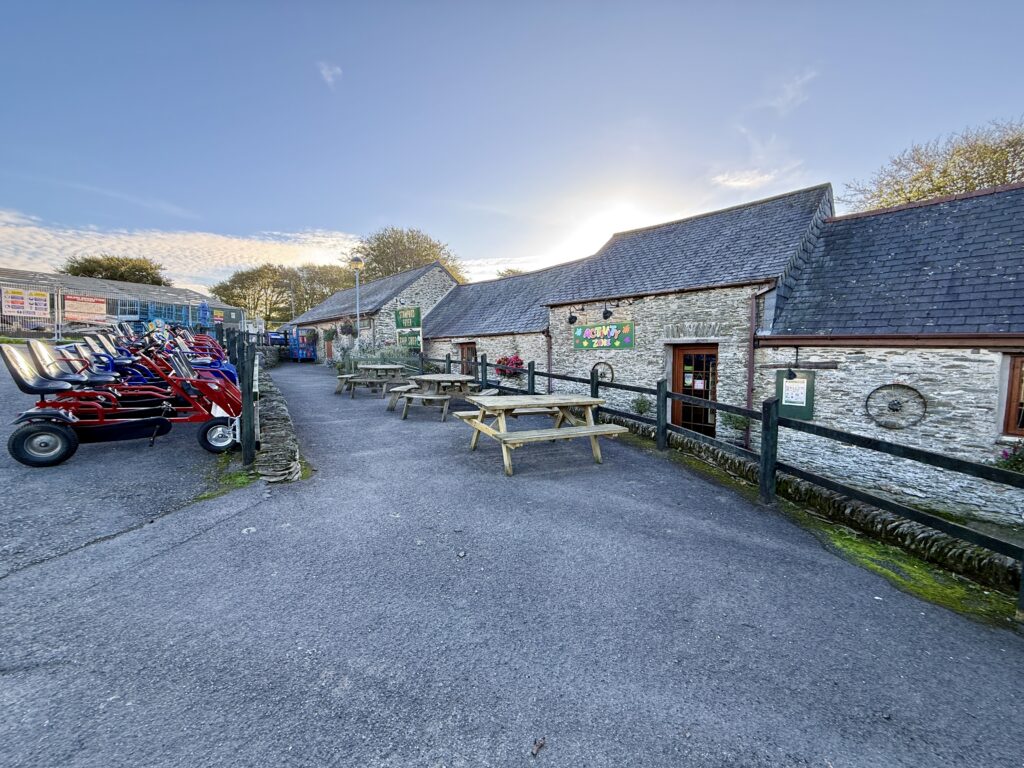 Activity area at Stowford Farm Meadows with stone buildings, outdoor picnic tables and pedal go-karts.