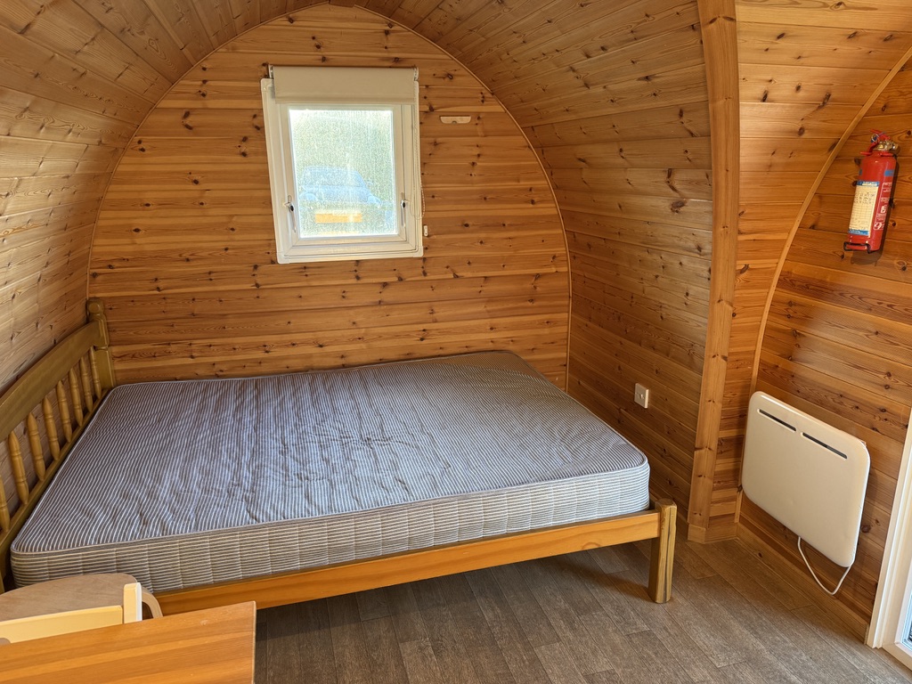 Double bed and electric wall heater inside a wood-panelled camping pod at Stowford Farm Meadows.