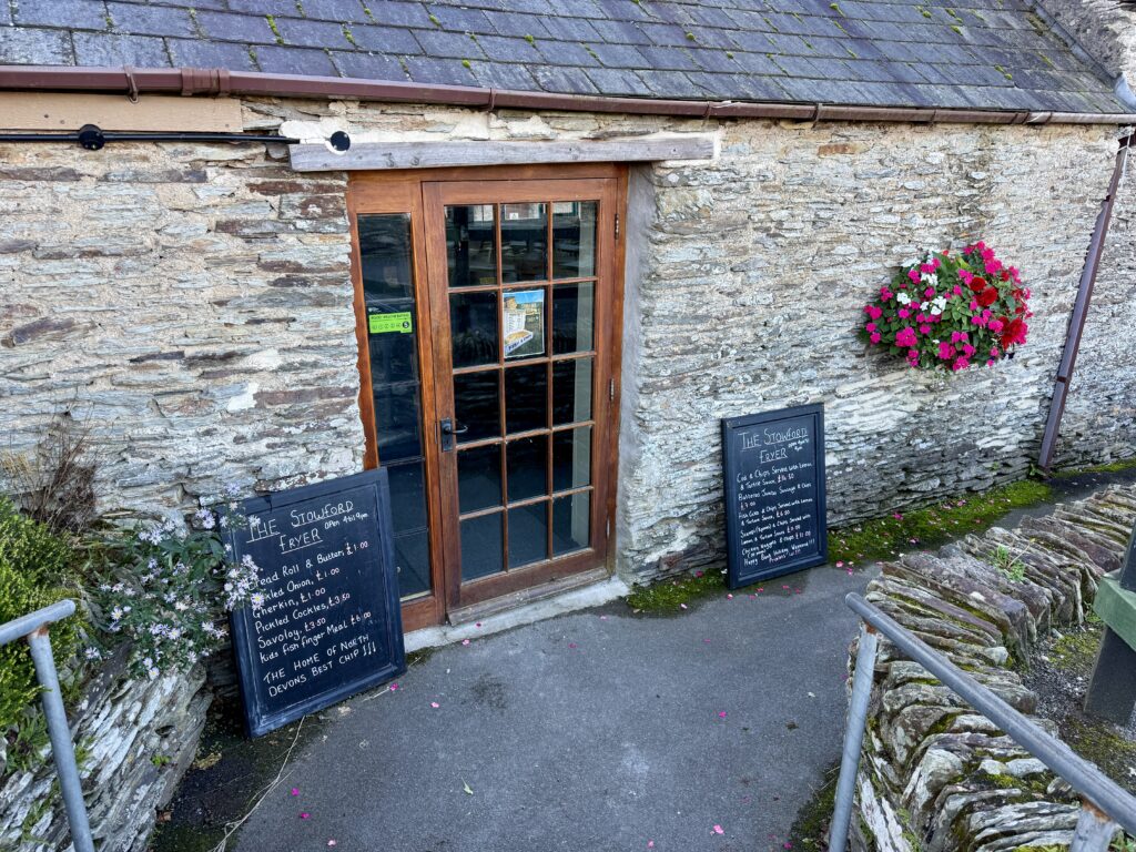 Stone-built Stowford Fryer fish and chip shop at Stowford Farm Meadows with menu boards beside the entrance.