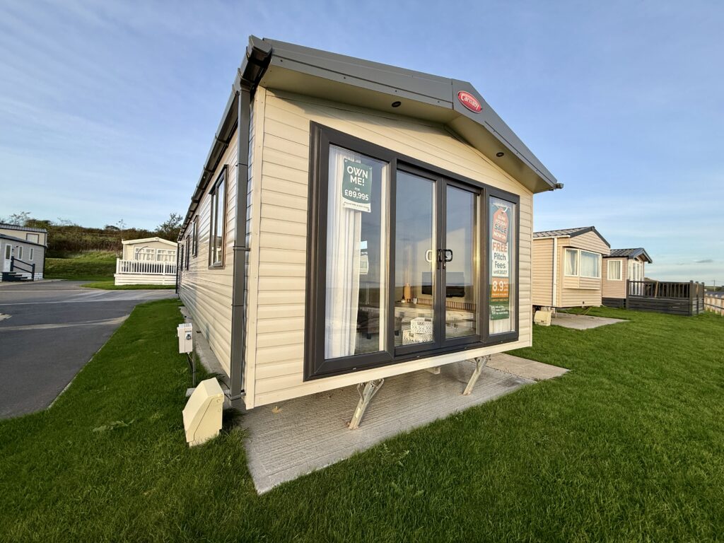 Modern static holiday caravan for sale at Stowford Farm Meadows with large front windows and surrounding grass pitch.