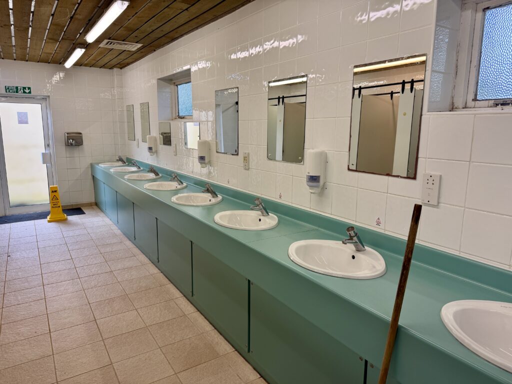 Clean mens communal washroom at Stowford Farm Meadows with a row of sinks, mirrors and tiled floors