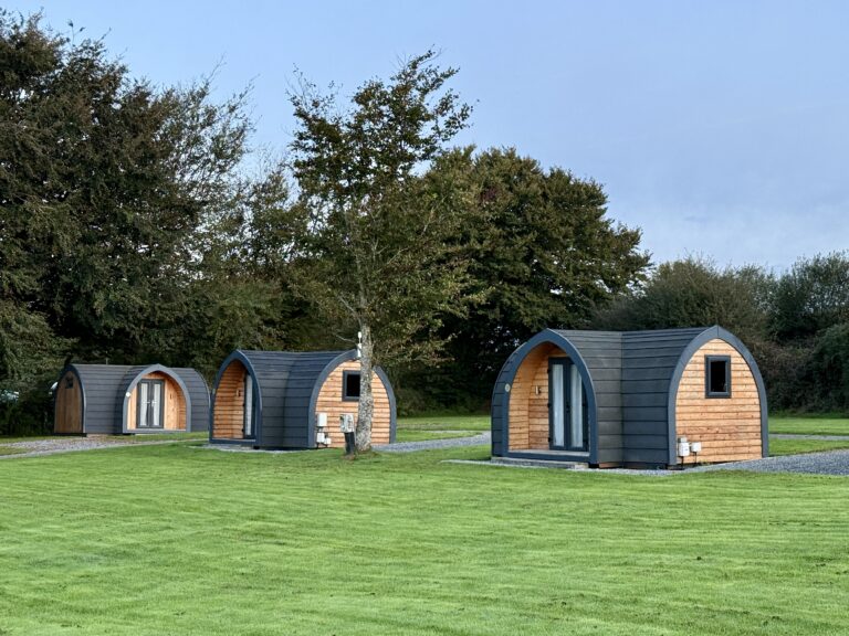 Wooden camping pods spaced across a large grass field surrounded by trees at Stowford Farm Meadows in North Devon